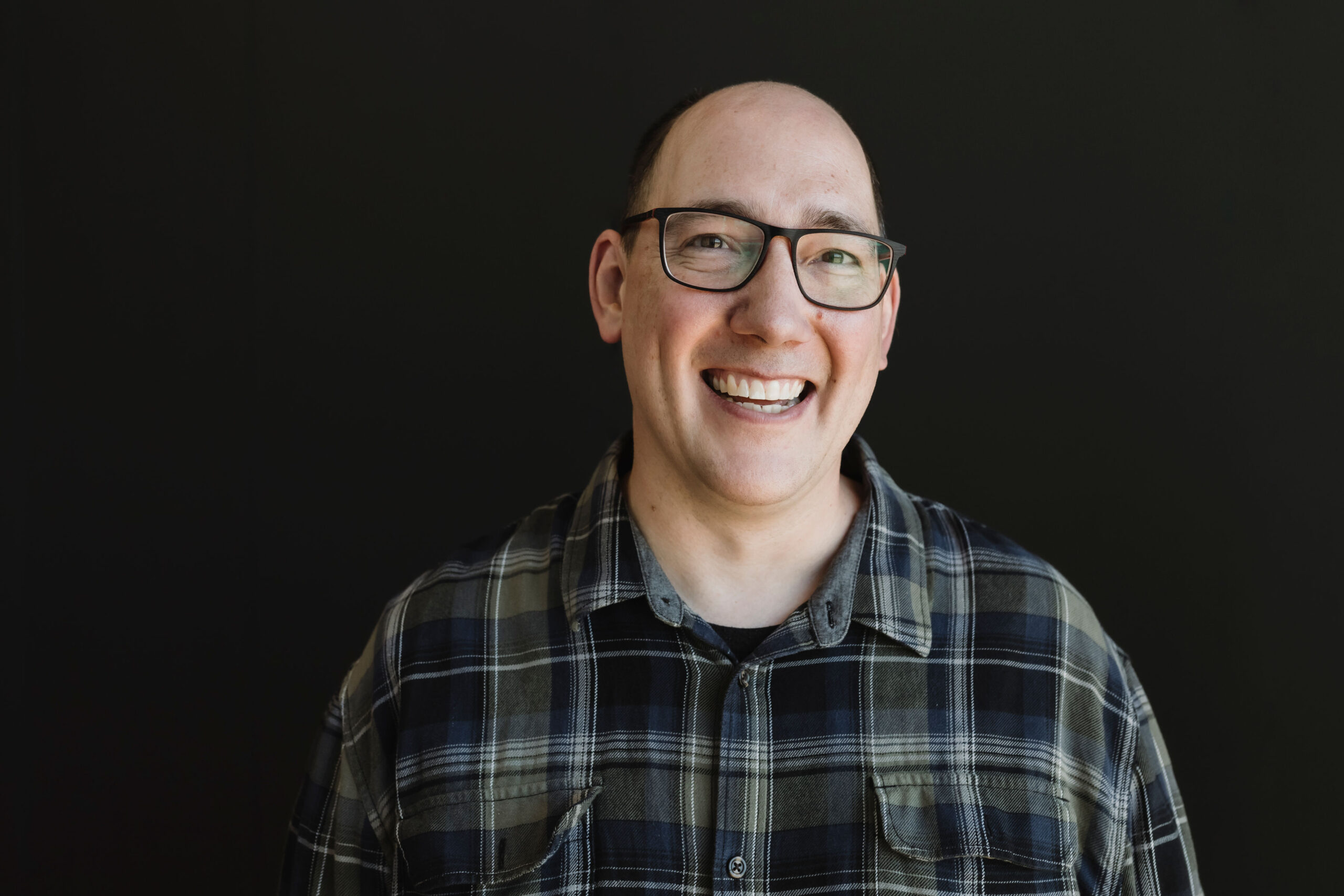 Composer Darren Miller smiles as he stands against a black background.