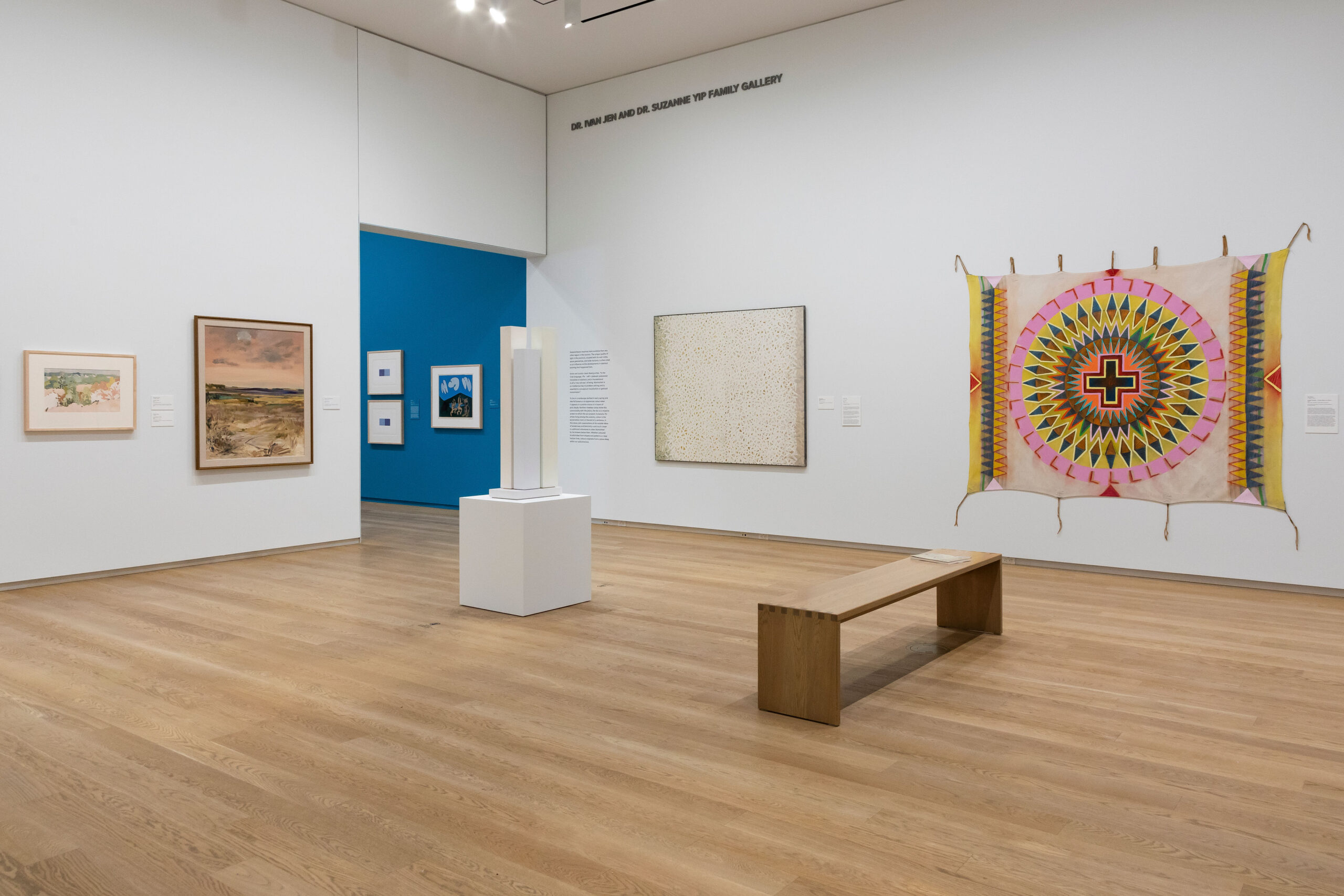 An art gallery room shows art hung on the wall, as well as a bench and sculpture on the floor.