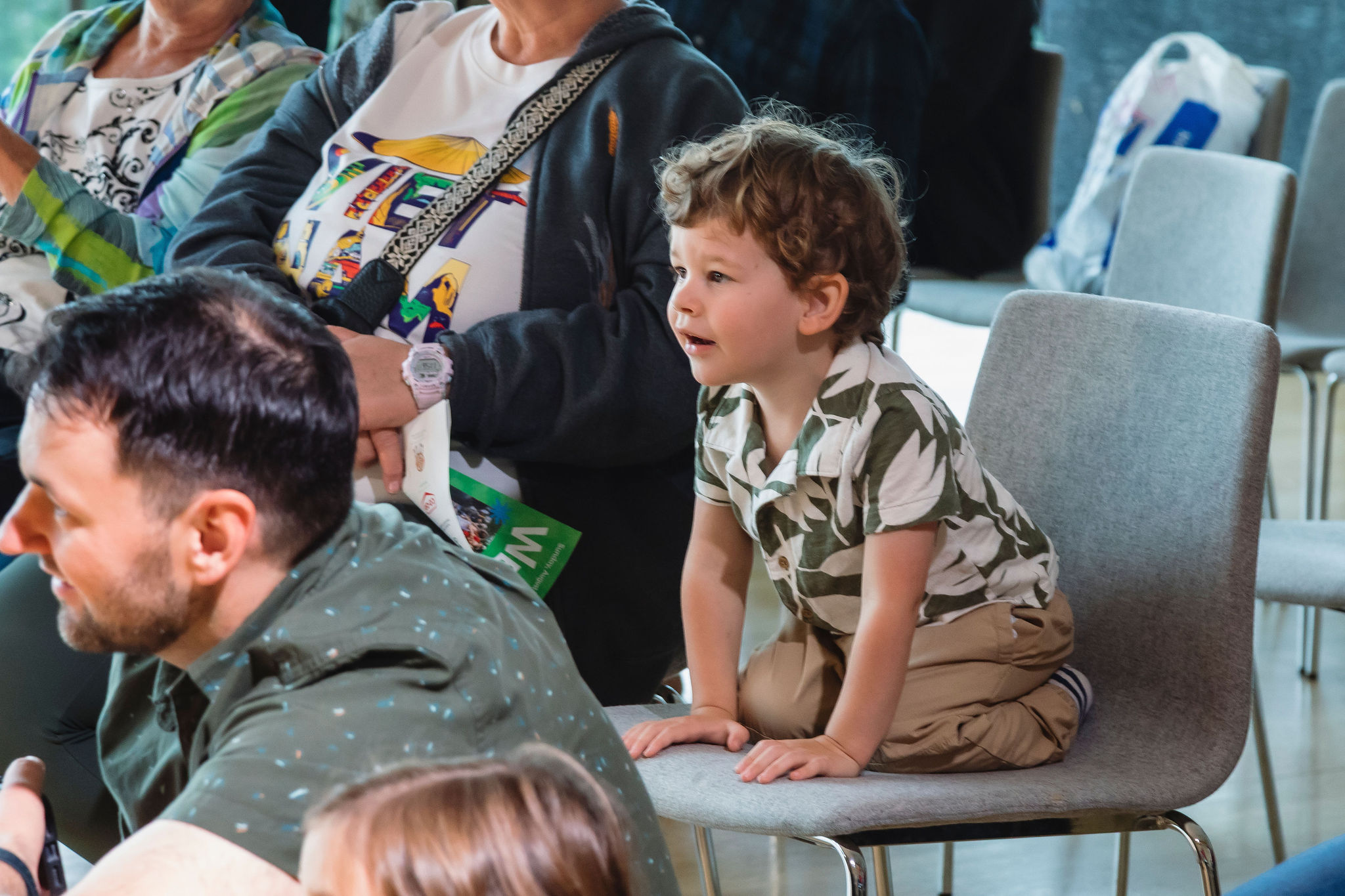 A young child kneels up on a chair in an audience, watching something intently off camera.