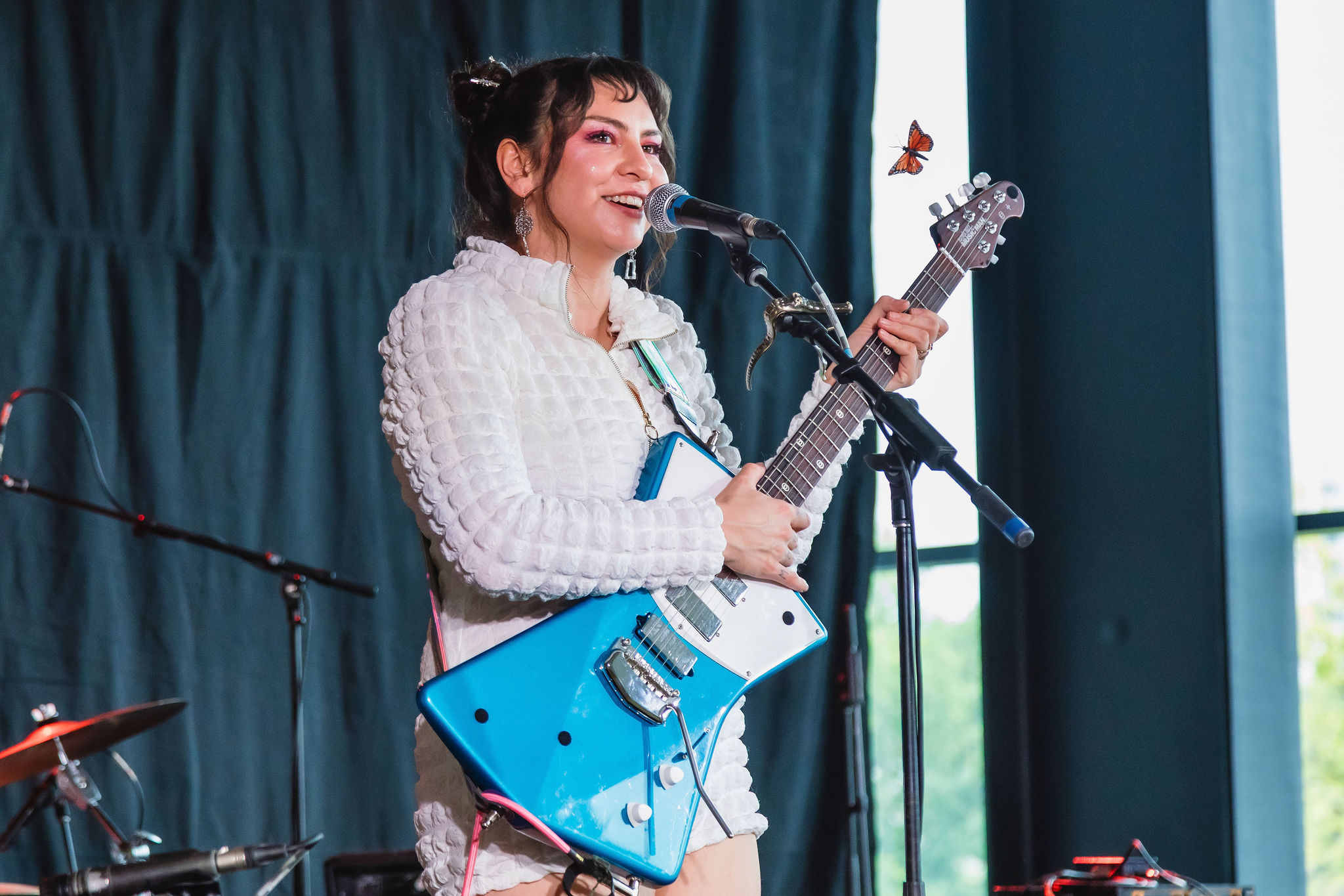 A performer sings into a microphone while playing a bright blue electric guitar on stage.