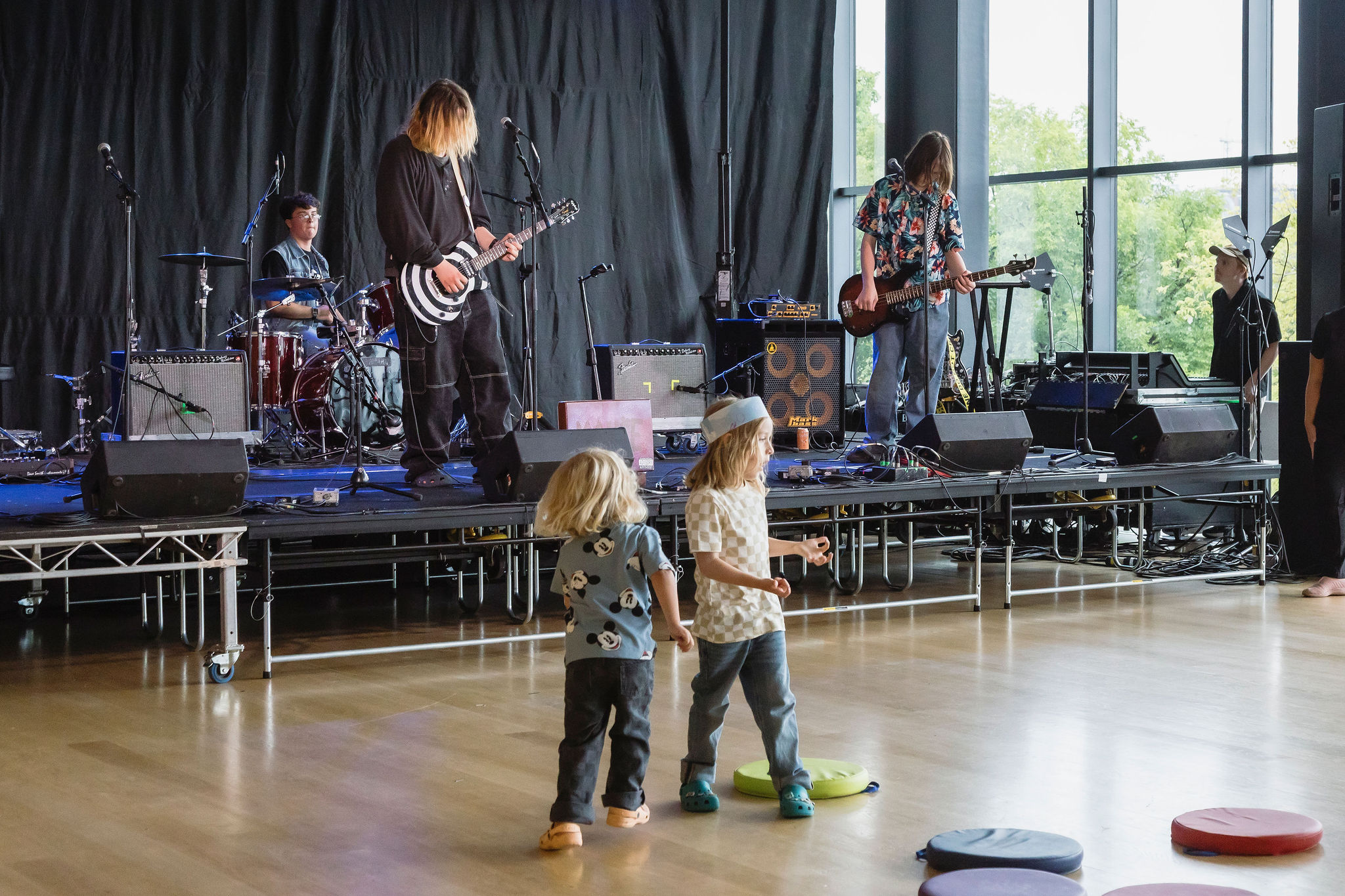 Two young children dance in front of a band playing on a low indoor stage.